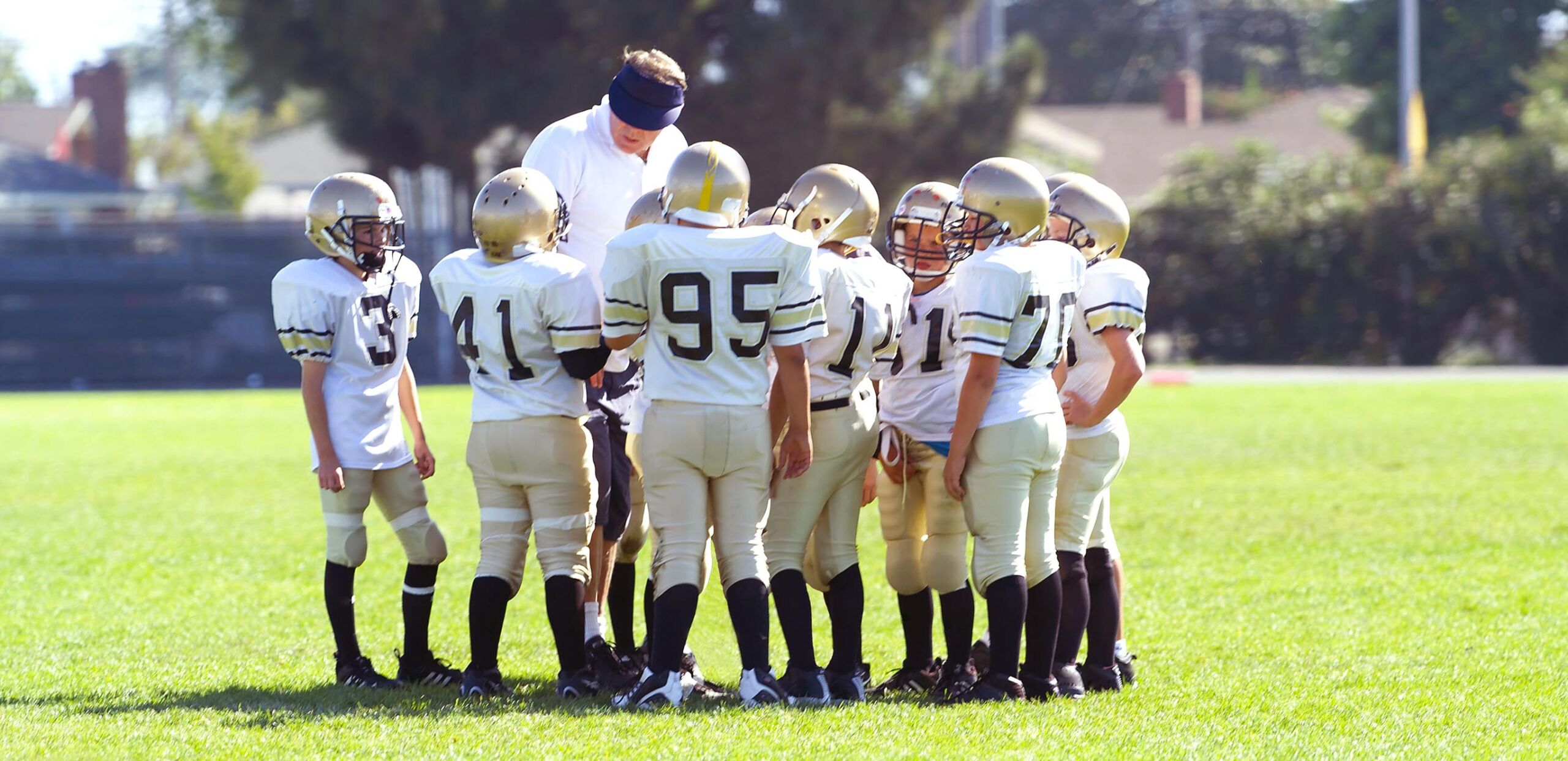 Elementary school football players huddle with their coach.