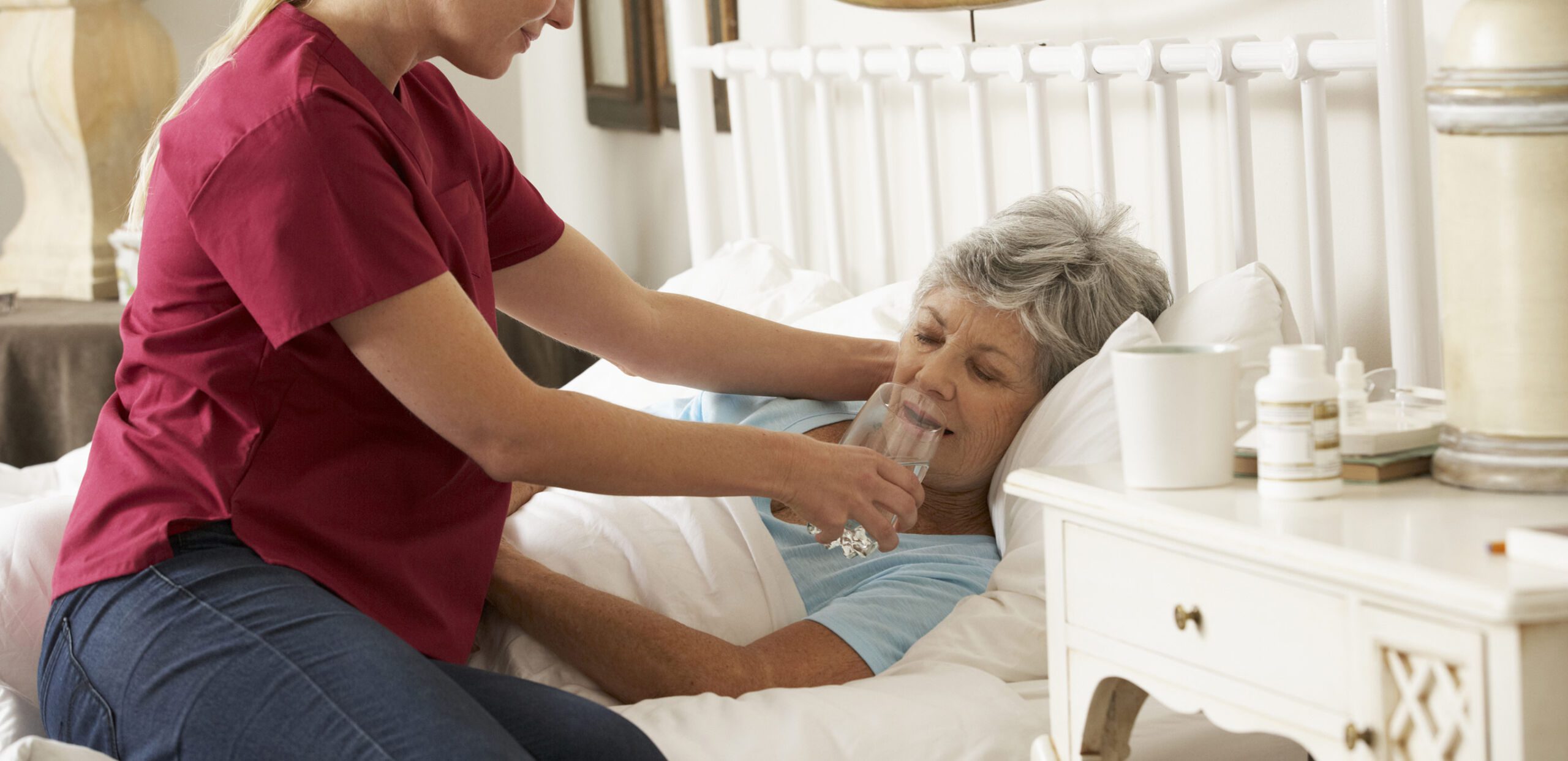 A palliative care provider helps a bed-bound patient take a sip of water from a glass in her home, Cooley Dickinson Medical Group VNA & Hospice, Northampton, MA 01060.