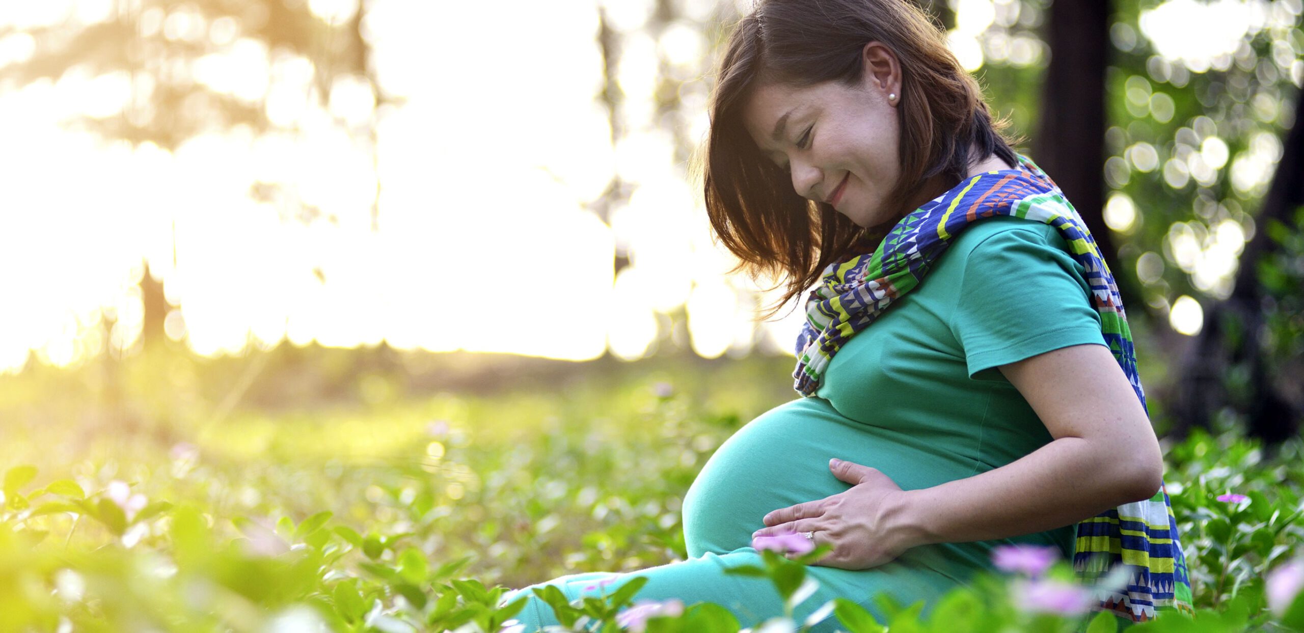 Smiling pregnant woman presses her hand against her belly.