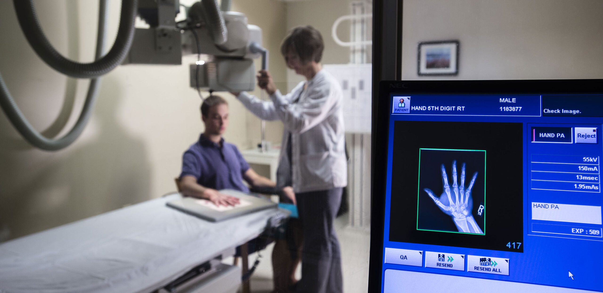 Workstation view of technologist preparing young man's hand for X-ray imaging at Cooley Dickinson Hospital, 30 Locust Street, Northampton, MA 01060.