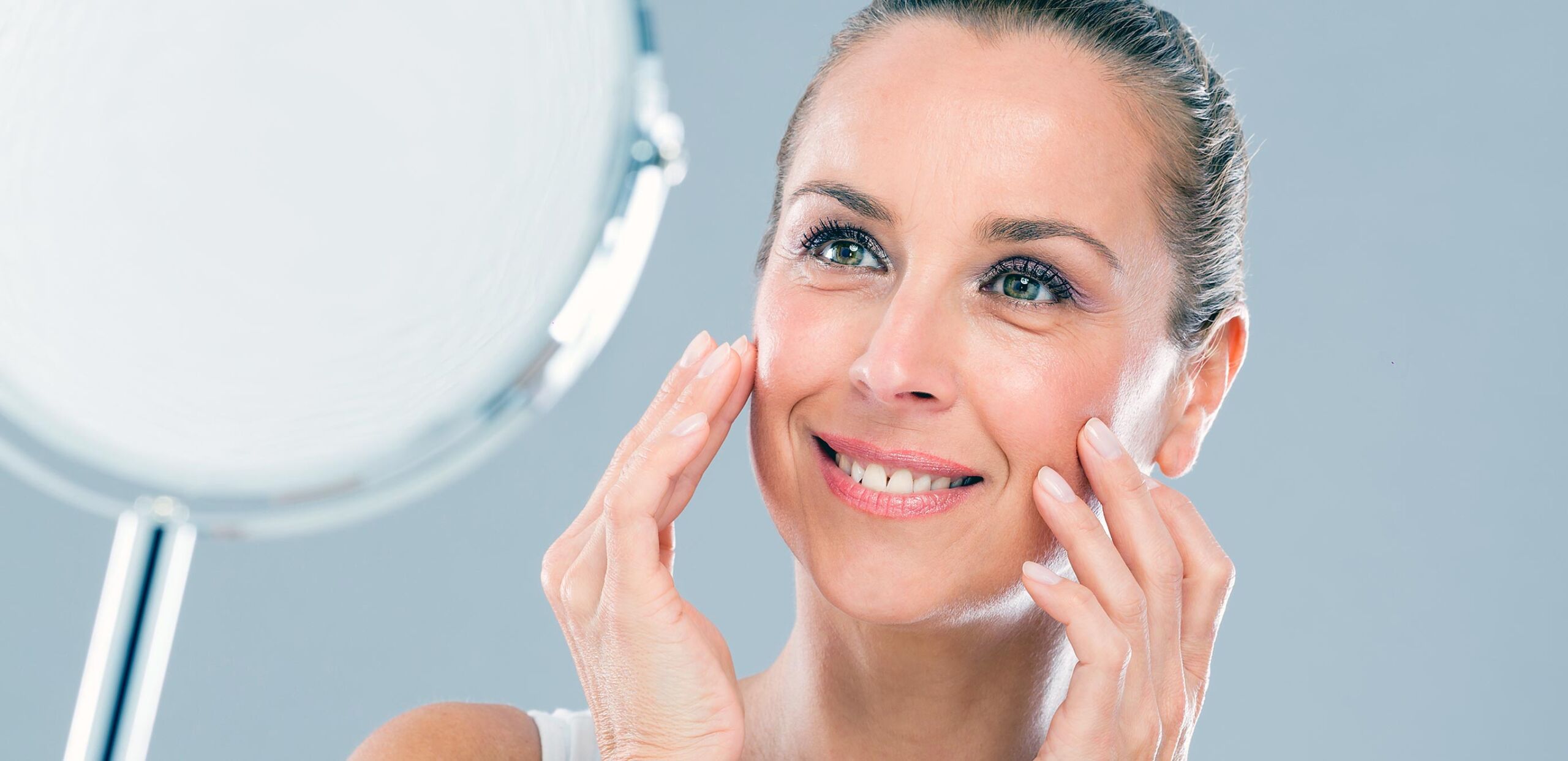 A woman smiles at her reflection after a procedure performed by Cooley Dickinson Medical Group Plastic Surgery, Florence, MA 01062.