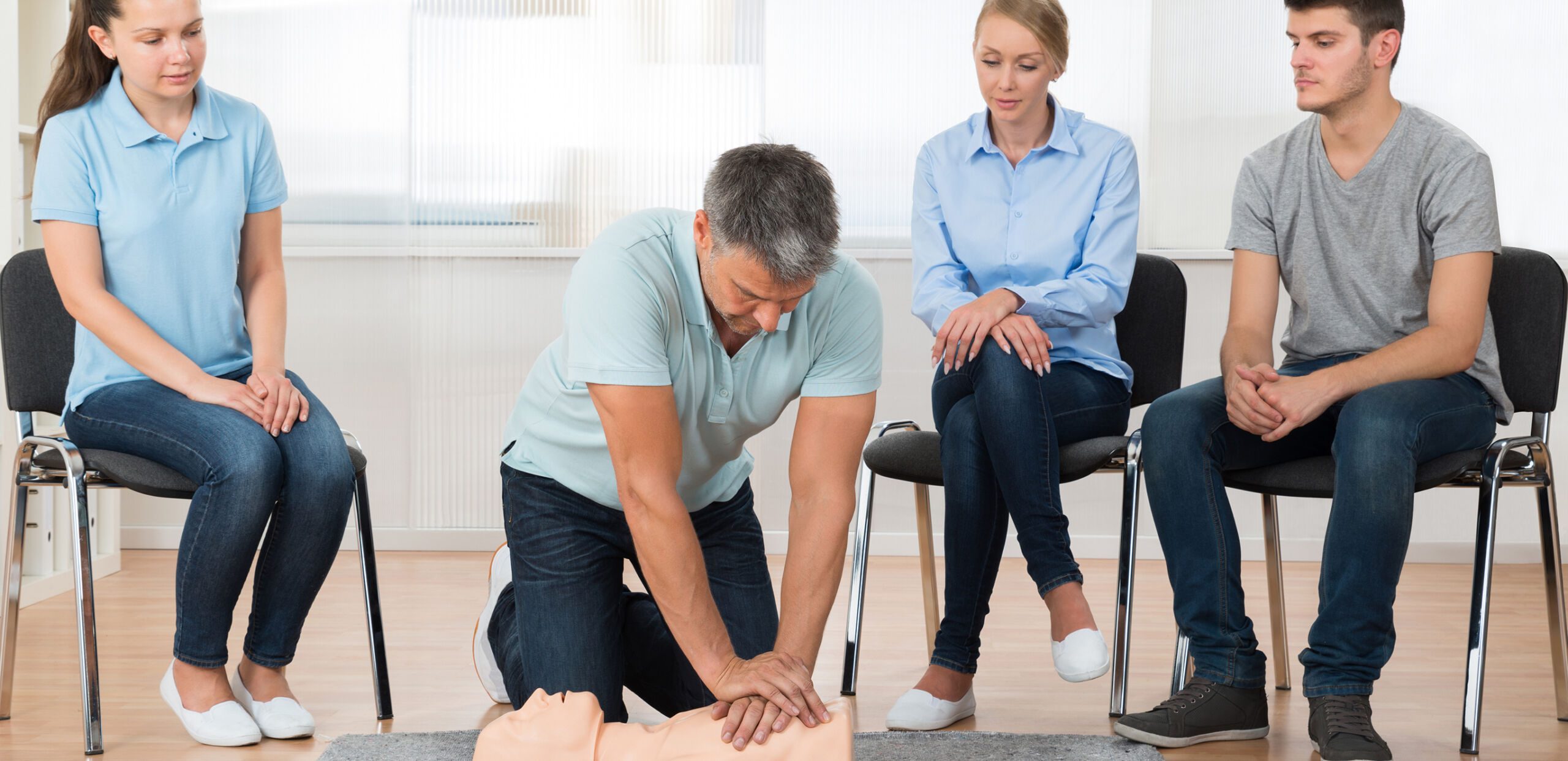 Male instructor teaching First Aid and CPR techniques to adult students.