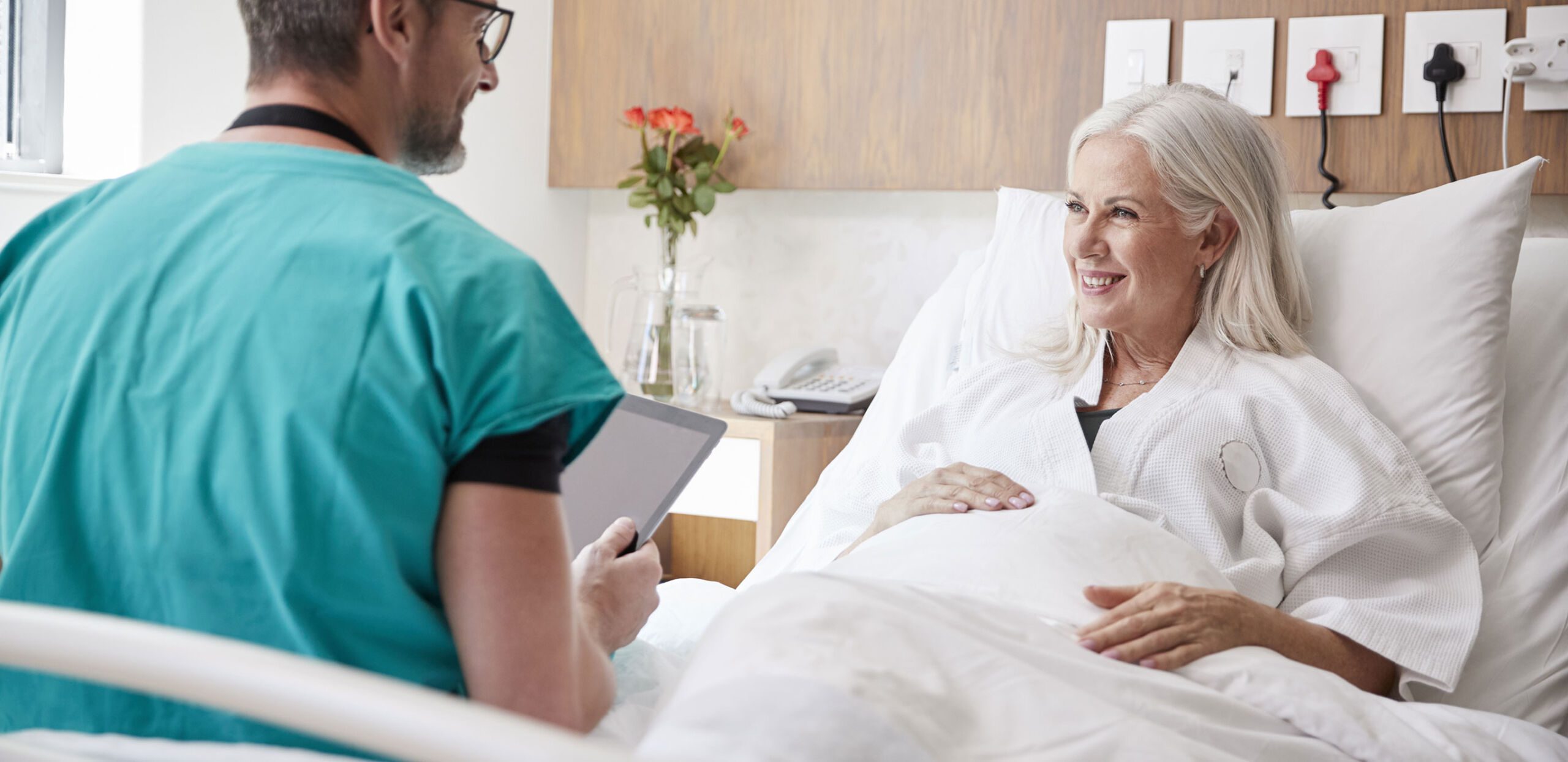 Older female patient in hospital bed speaking to a medical provider