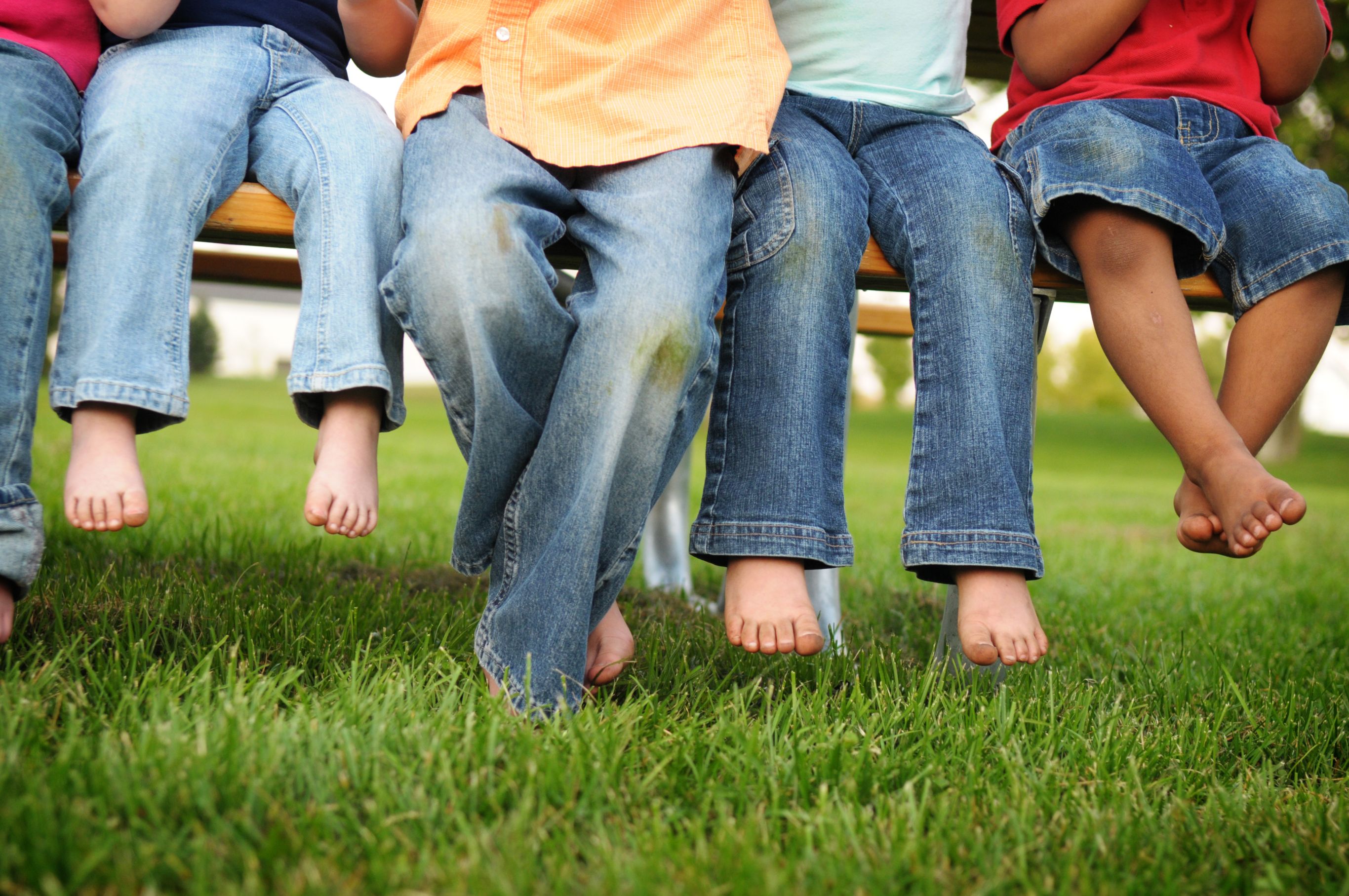 Color photo of the bare feet of little kids sitting on a picnic table.