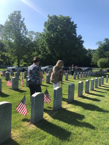 Karen Miller digs the hole for the flag to be placed, while Ashley Watt waits to place the flag in front of the grave.  In the background is Tina Leflar carrying more flags to be placed.