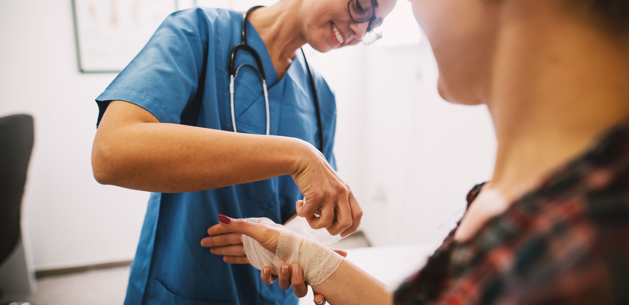 Smiling nurse placing a bandage on the wrist of a patient.