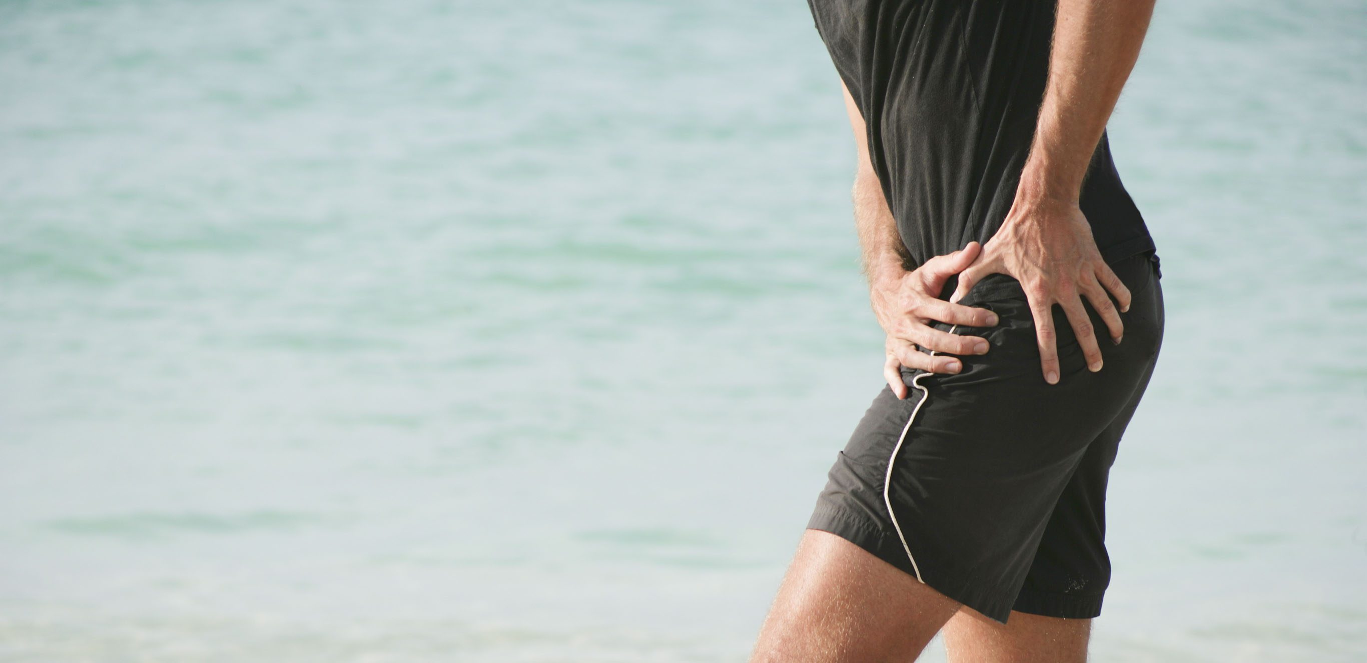 man clutching his hip while walking on the beach